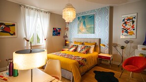Ein modernes Schlafzimmer mit einem großen Bett, einem Schreibtisch mit Lampe, einem roten Sessel und Bildern an den Wänden.