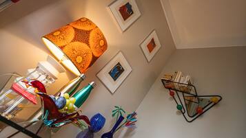 Een kamer met een lamp, afbeeldingen aan de muur en een klein boekenrek.
