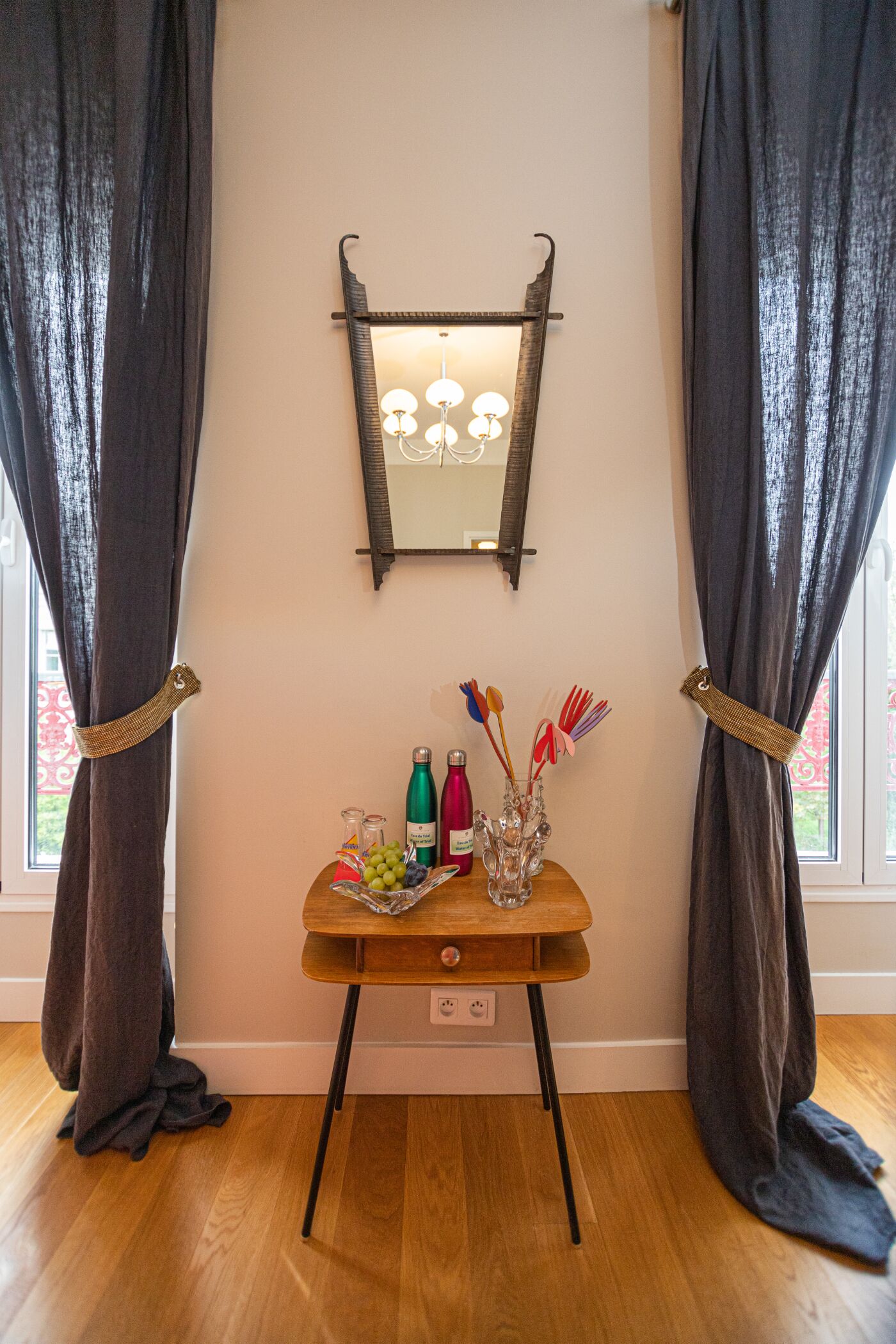 A room with a wooden table against a wall, a mirror above it, and a window with curtains.