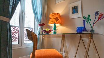 Une pièce comprenant une chaise en bois, une table en verre, une lampe et des œuvres d’art accrochées au mur.