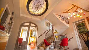Ein geräumiger Eingangsbereich mit Treppe, roten Stühlen, einer runden Deckenleuchte und einem Kronleuchter.
