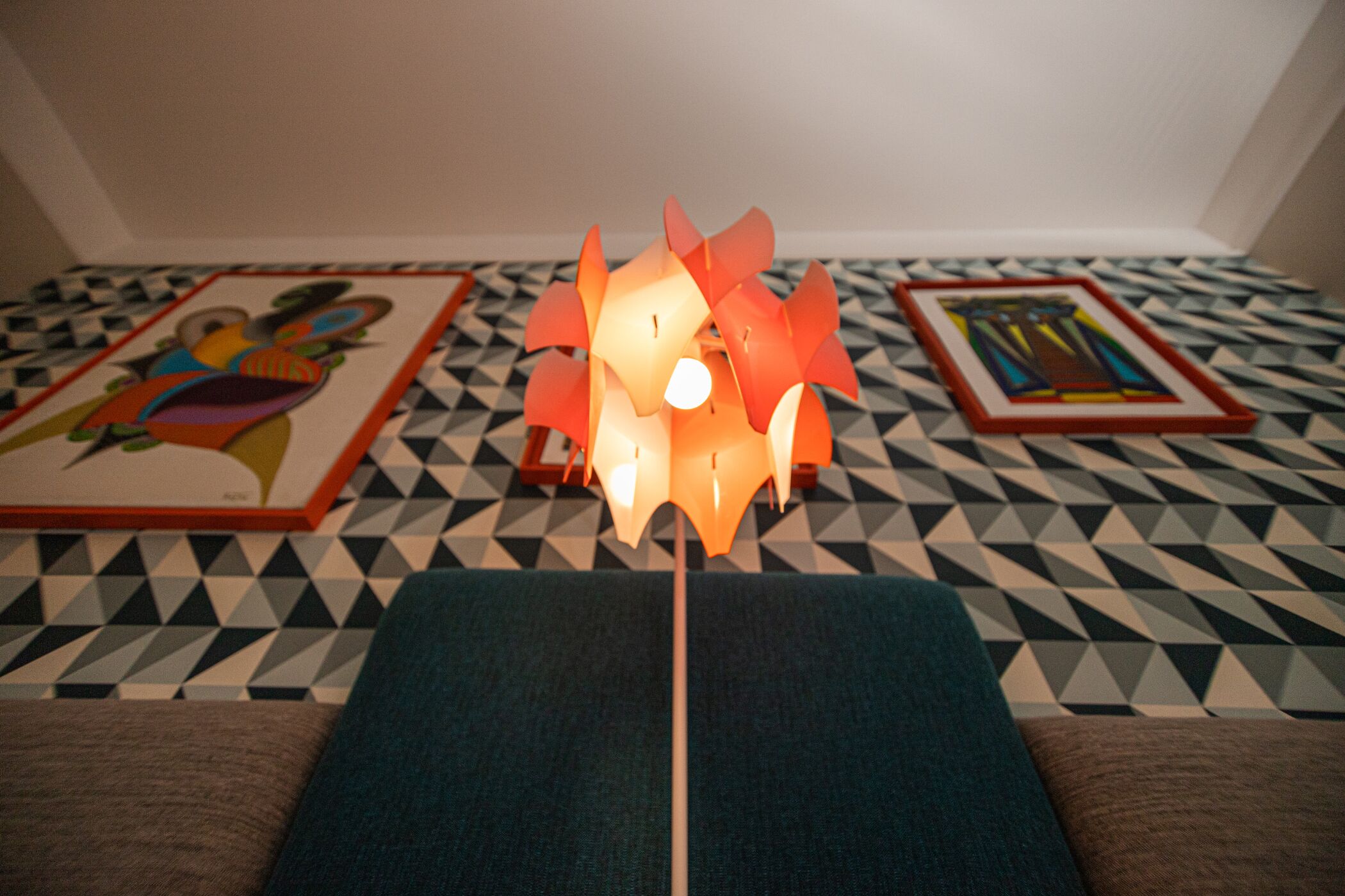 Ein Zimmer mit einem geometrisch gemusterten Boden, einer zentralen Leuchte und zwei gerahmten Kunstwerken an den Wänden.