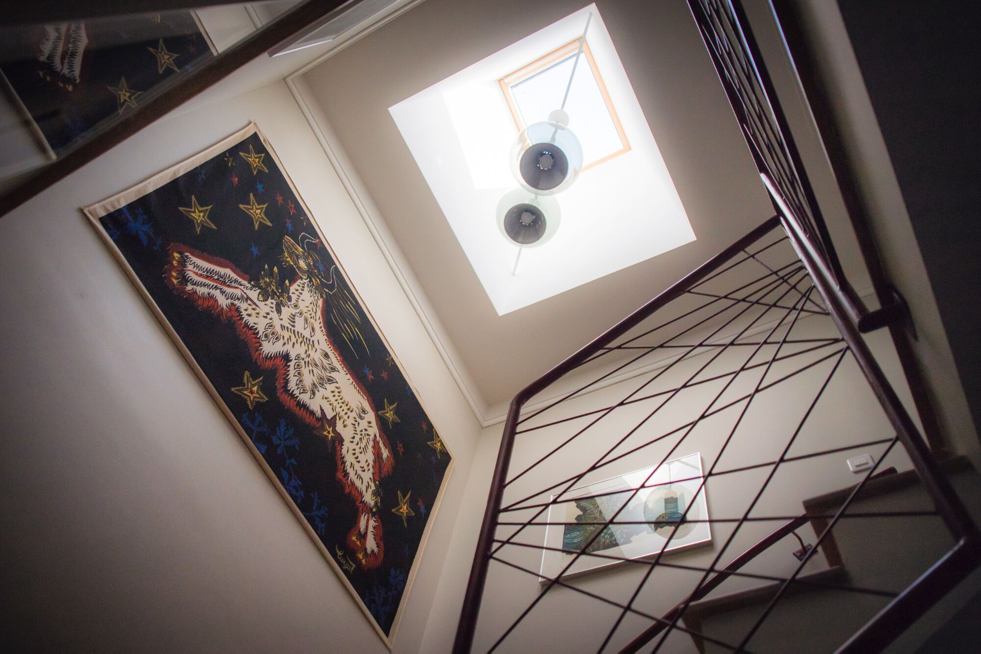 A staircase with a metal railing, a framed artwork on the wall, and a window with a geometric design.