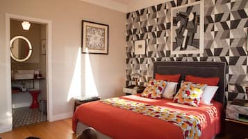 Une chambre à coucher avec un grand lit, une table de chevet, une commode, un miroir et un mur orné d’un motif géométrique.