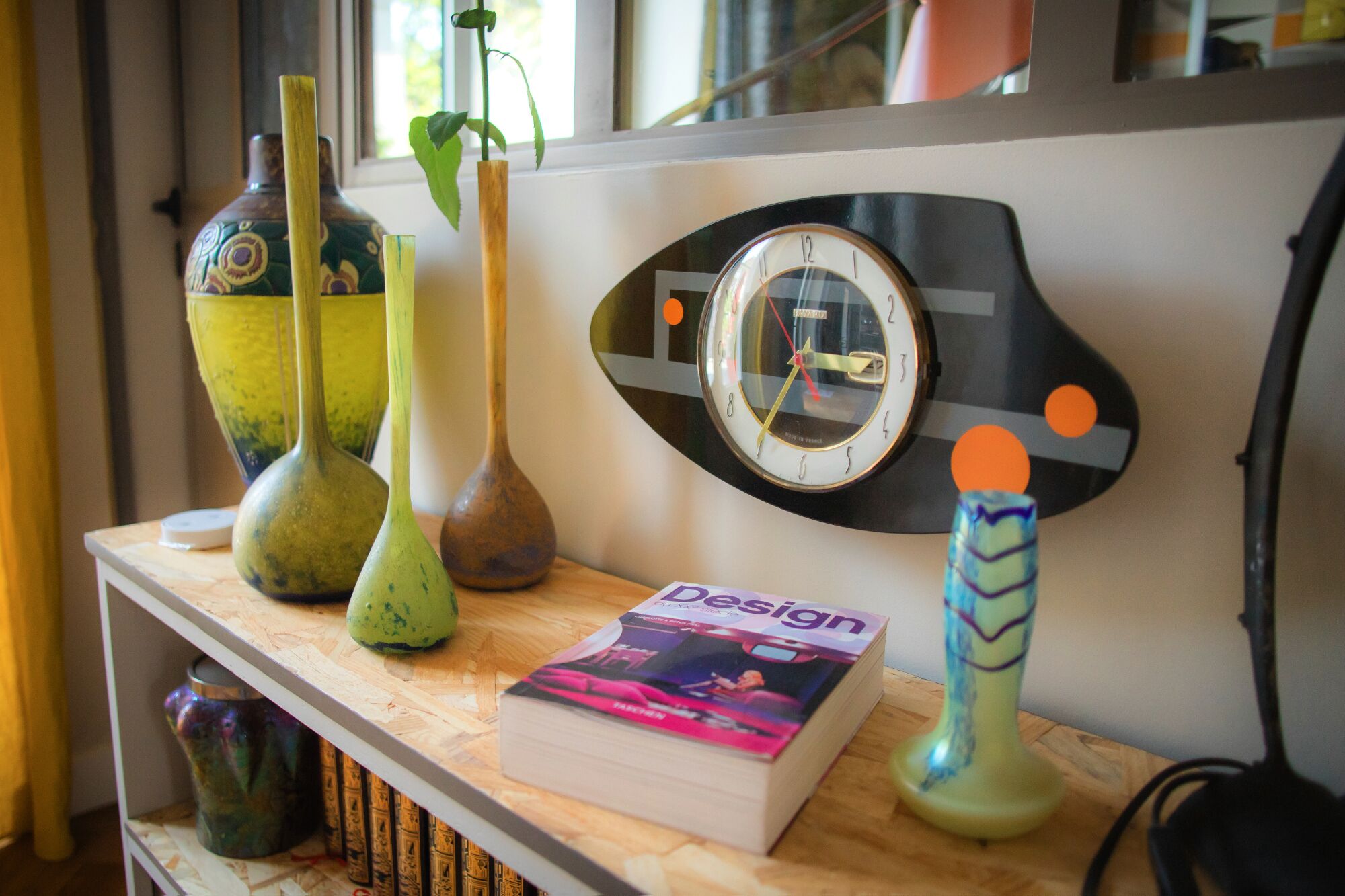 A shelf with decorative vases, a book titled 'Design', and a wall clock.