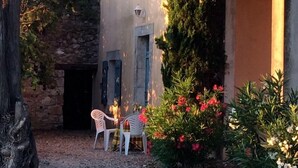 A rustic courtyard with stone walls, a wooden door, and a small table with chairs. - Gîtes Pech-céleyran (Salles-d'Aude)