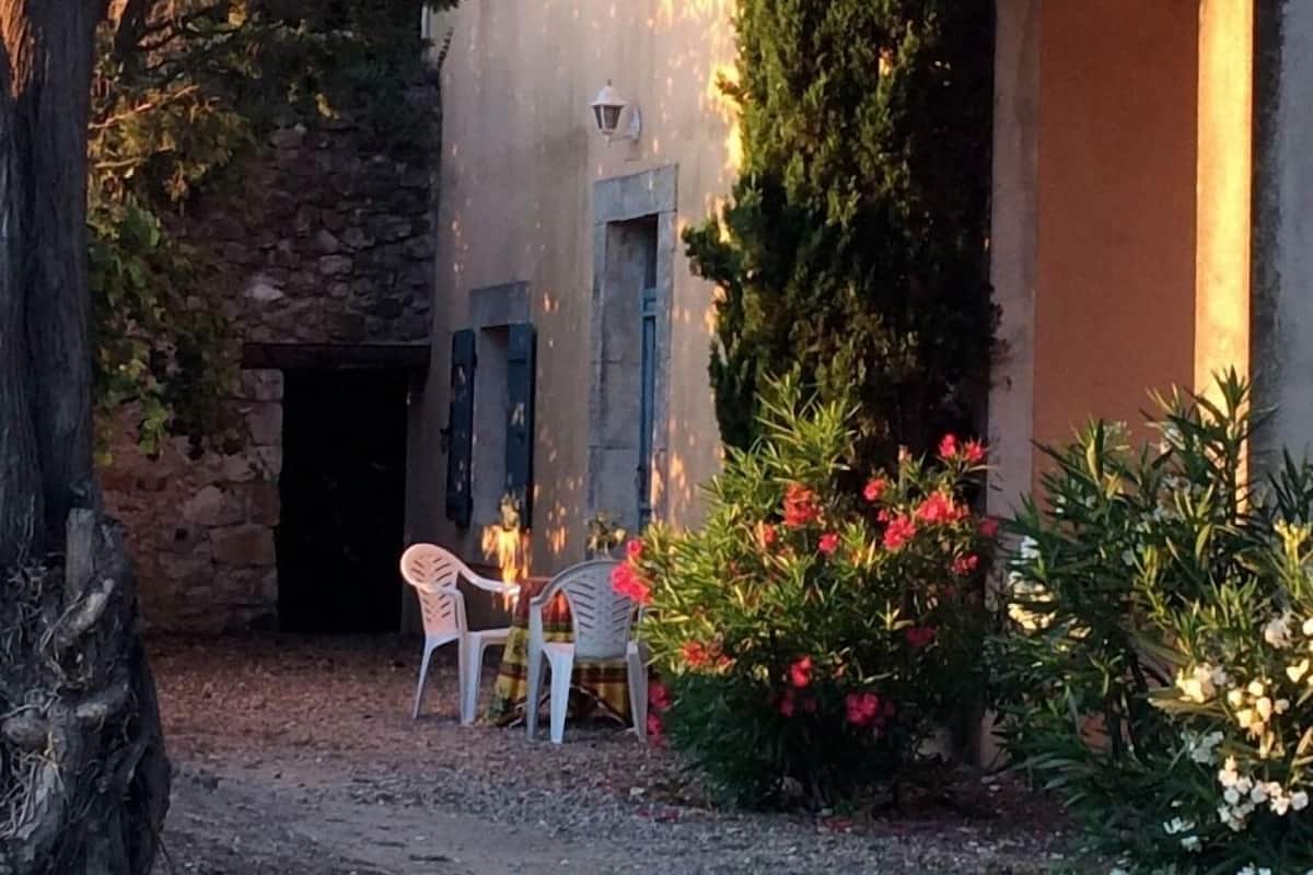 Une cour rustique avec des murs en pierre, une porte en bois et une petite table entourée de chaises.