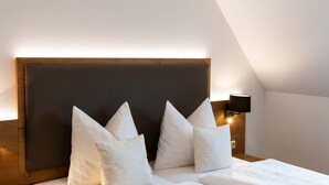 A neatly made bed with white linens and pillows, a wooden headboard, and a wall-mounted light fixture. - Hotel Gasthof Rosenwirt (Au in der Hallertau)