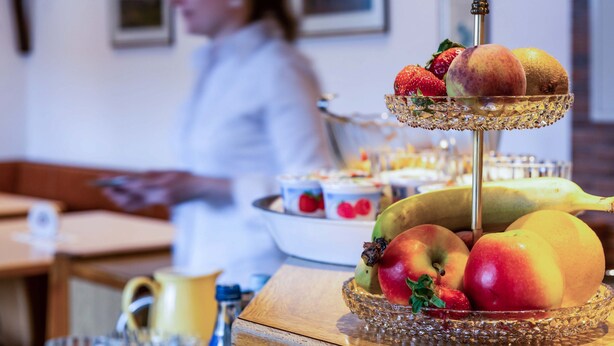 A breakfast setting with a fruit display, a cake, and a person in the background. - Hotel Gasthof Rosenwirt (Au in der Hallertau)
