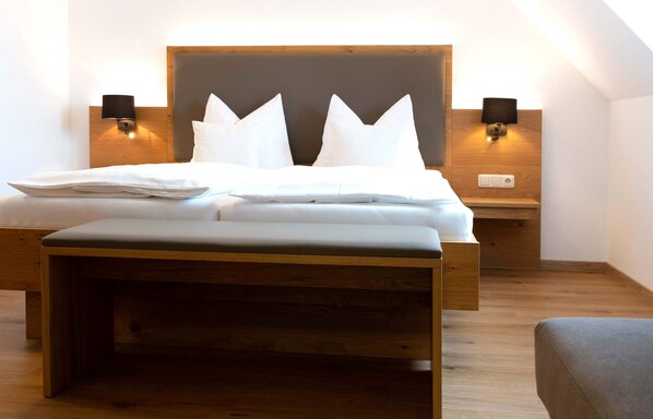 A neatly made bed with a wooden headboard, two bedside lamps, and a bench at the foot of the bed. - Hotel Gasthof Rosenwirt (Au in der Hallertau)