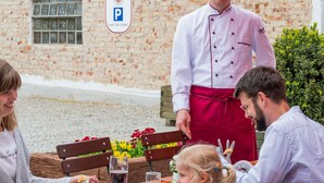 A chef standing by a table with a brick building in the background. - Hotel Gasthof Rosenwirt (Au in der Hallertau)