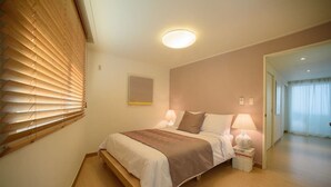 A neatly arranged bedroom with a bed, bedside lamps, and a window with blinds. - Stay Young (Seoul)