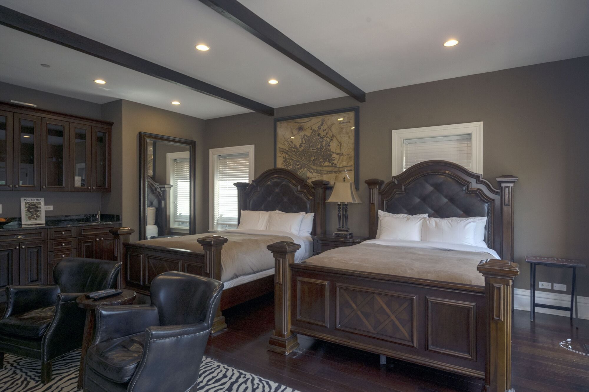 A bedroom with two large beds, a sitting area with chairs, a wooden desk, and a large map on the wall.