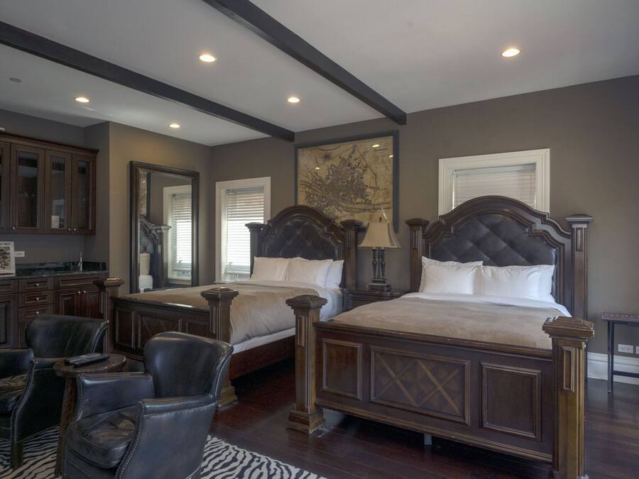 A bedroom with two large beds, a sitting area with chairs, a wooden desk, and a large map on the wall.