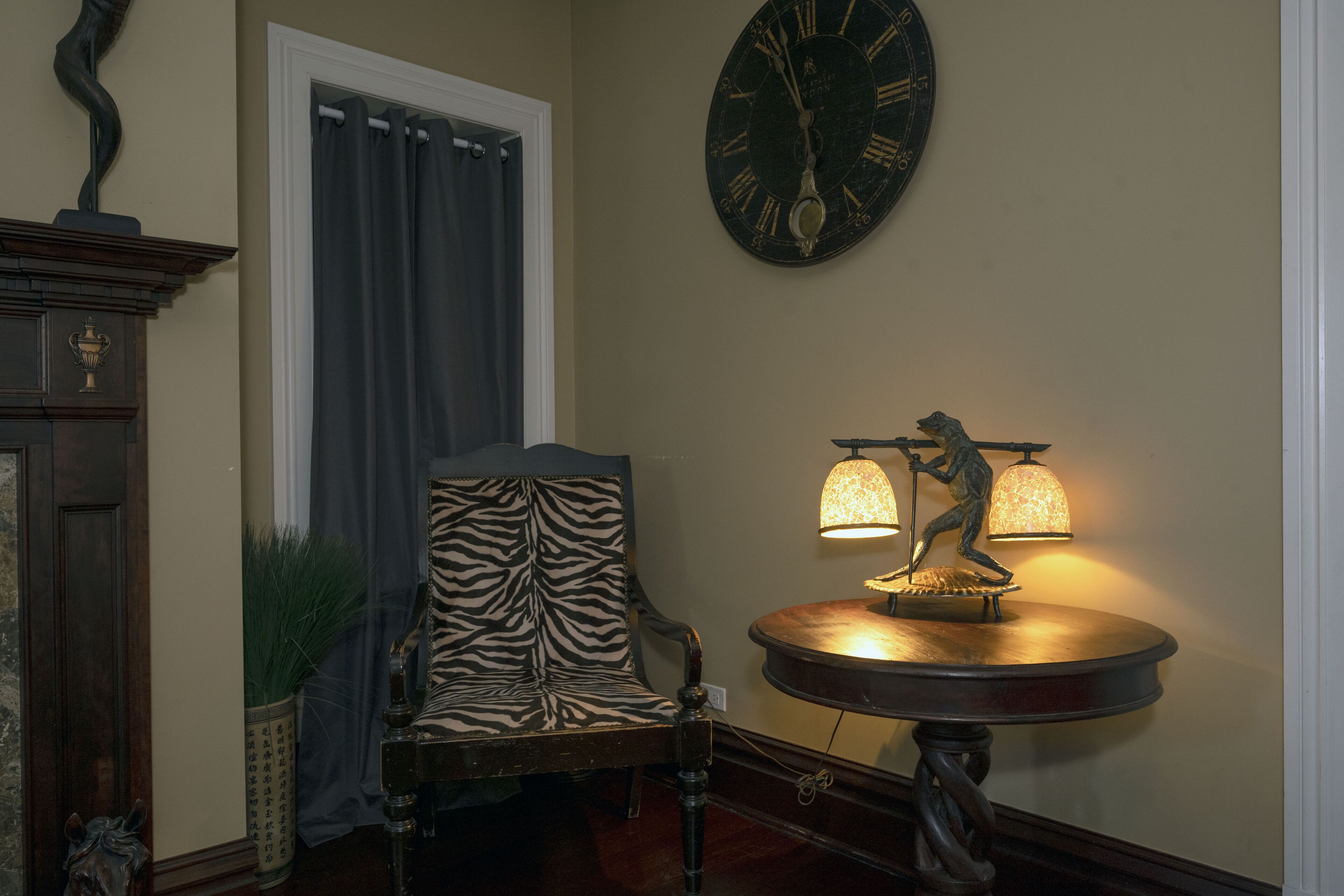 A room with a zebra-patterned chair, a wall clock, and a table lamp with a figure.