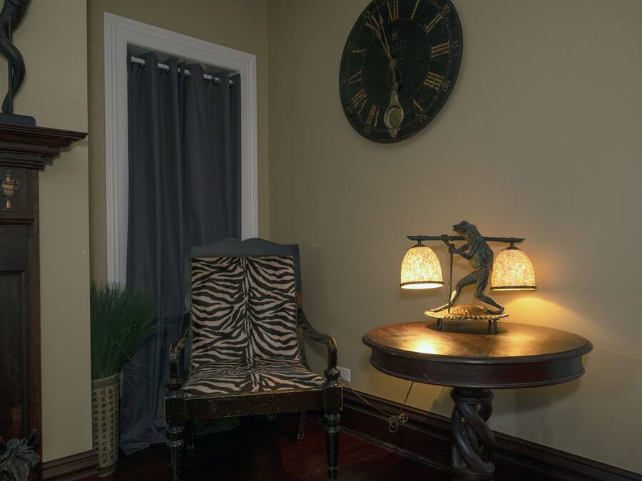 A room with a zebra-patterned chair, a wall clock, and a table lamp with a figure.