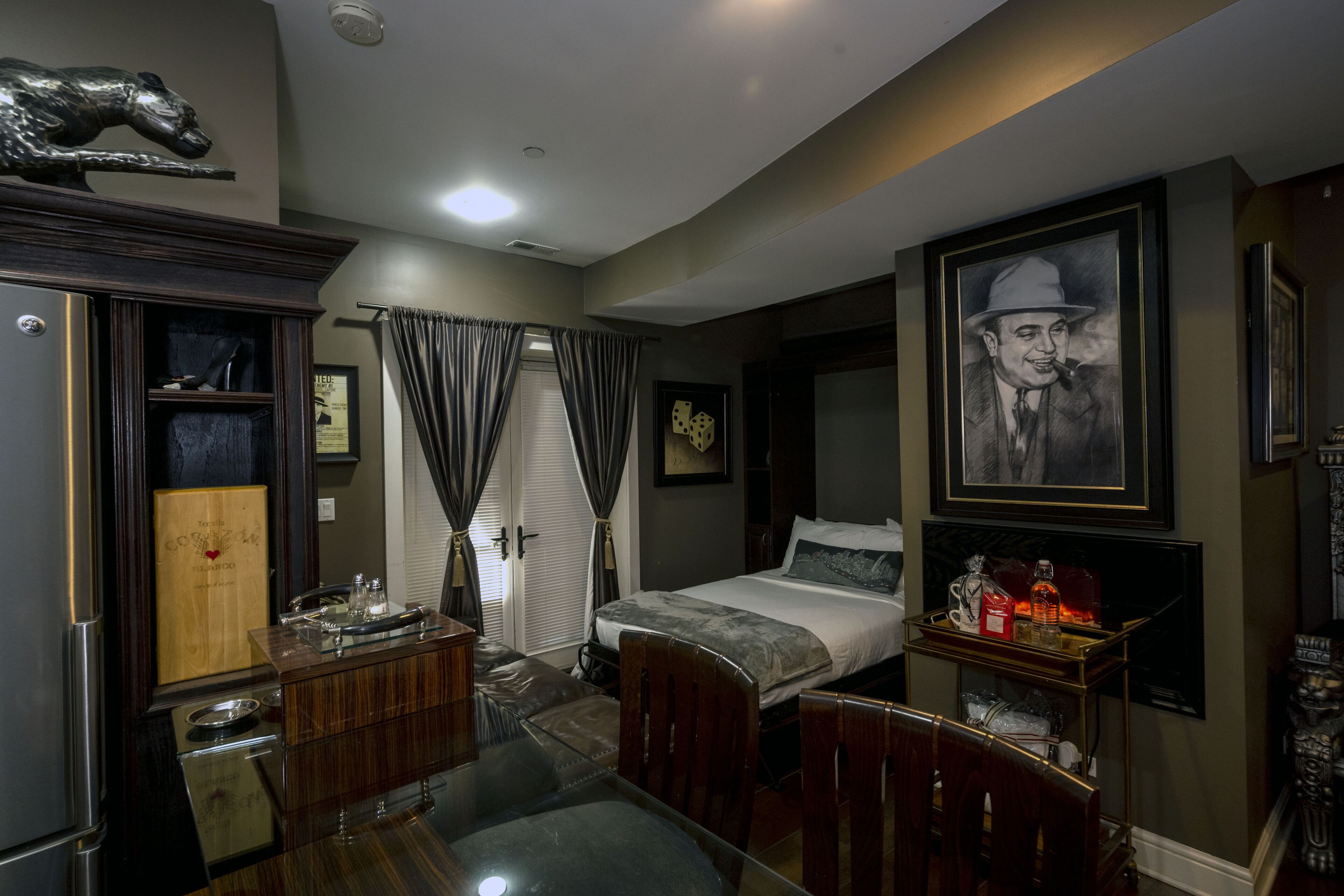 A hotel room with a bed, a desk, a chair, a small table, a refrigerator, and a cabinet.