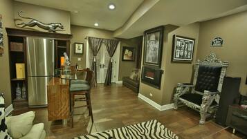 A spacious living room with a large wooden dining table, a sofa, a zebra-patterned rug, a fireplace, and a vintage armchair.