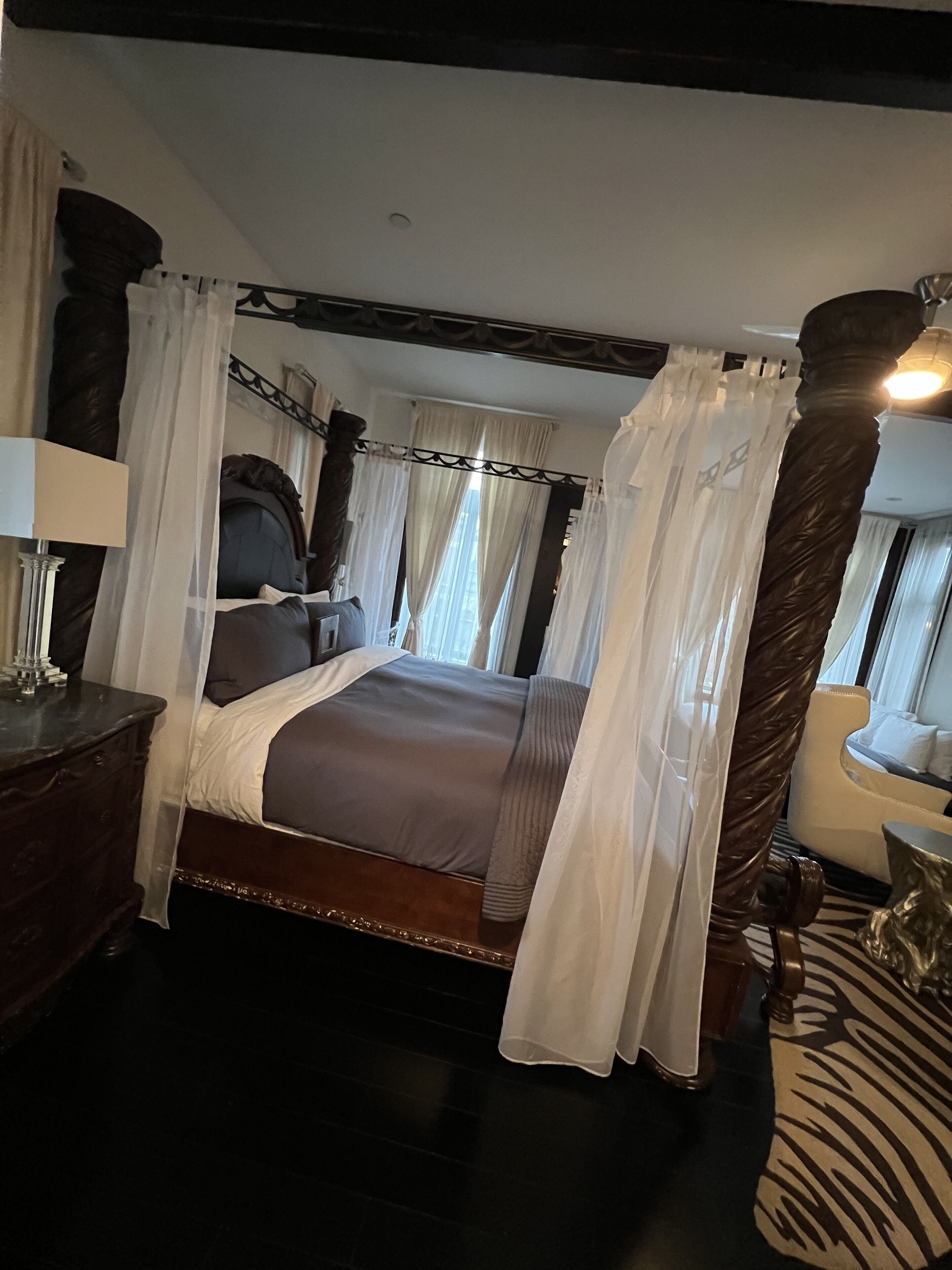 A bedroom with a four-poster bed, a nightstand, a lamp, and a zebra-patterned rug.