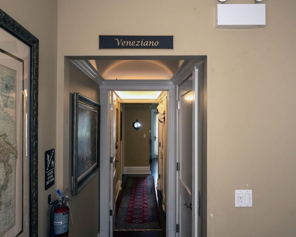 Corredor com uma placa indicando "Veneziano", um extintor de incêndio e um mapa emoldurado na parede.