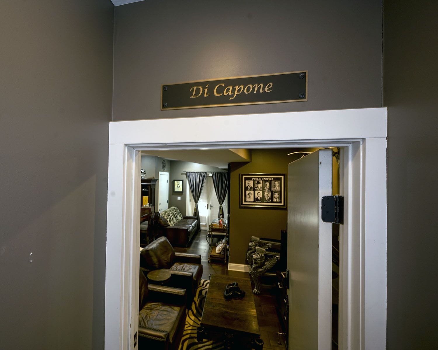 A doorway labeled "Di Capone" leading into a room with leather furniture, a zebra-patterned rug, and a framed picture on the wall.