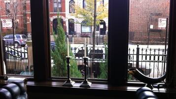 A view from a window with a black metal railing, a Christmas tree, and a building with a brick facade.