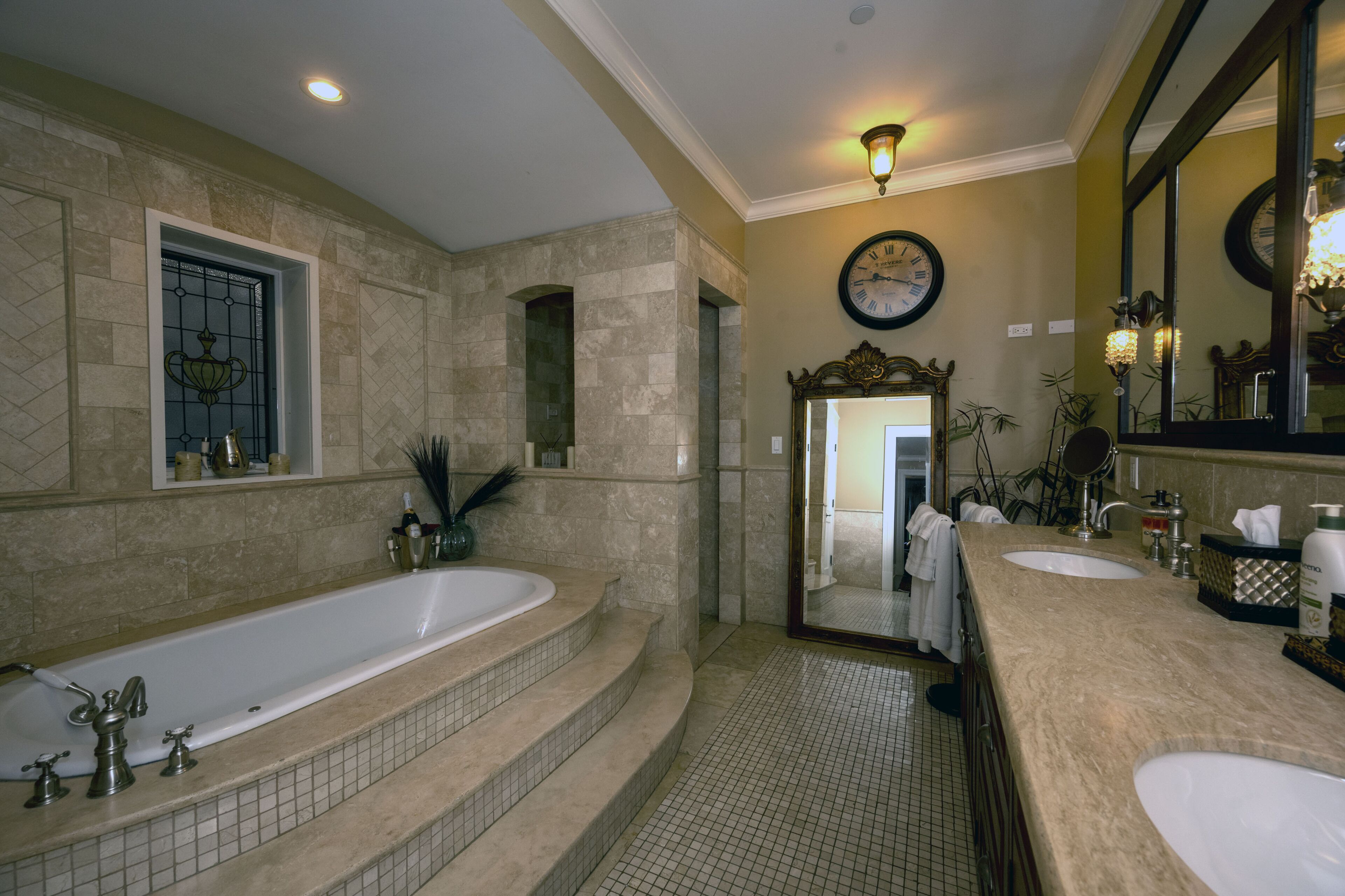 A bathroom with a large bathtub, two sinks, a mirror, and a clock on the wall.