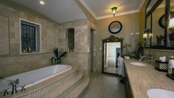A bathroom with a large bathtub, two sinks, a mirror, and a clock on the wall.