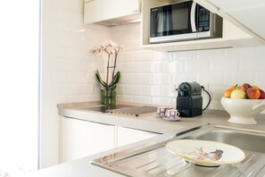 Cozinha moderna com armários brancos, micro-ondas, cafeteira e uma tigela de frutas.