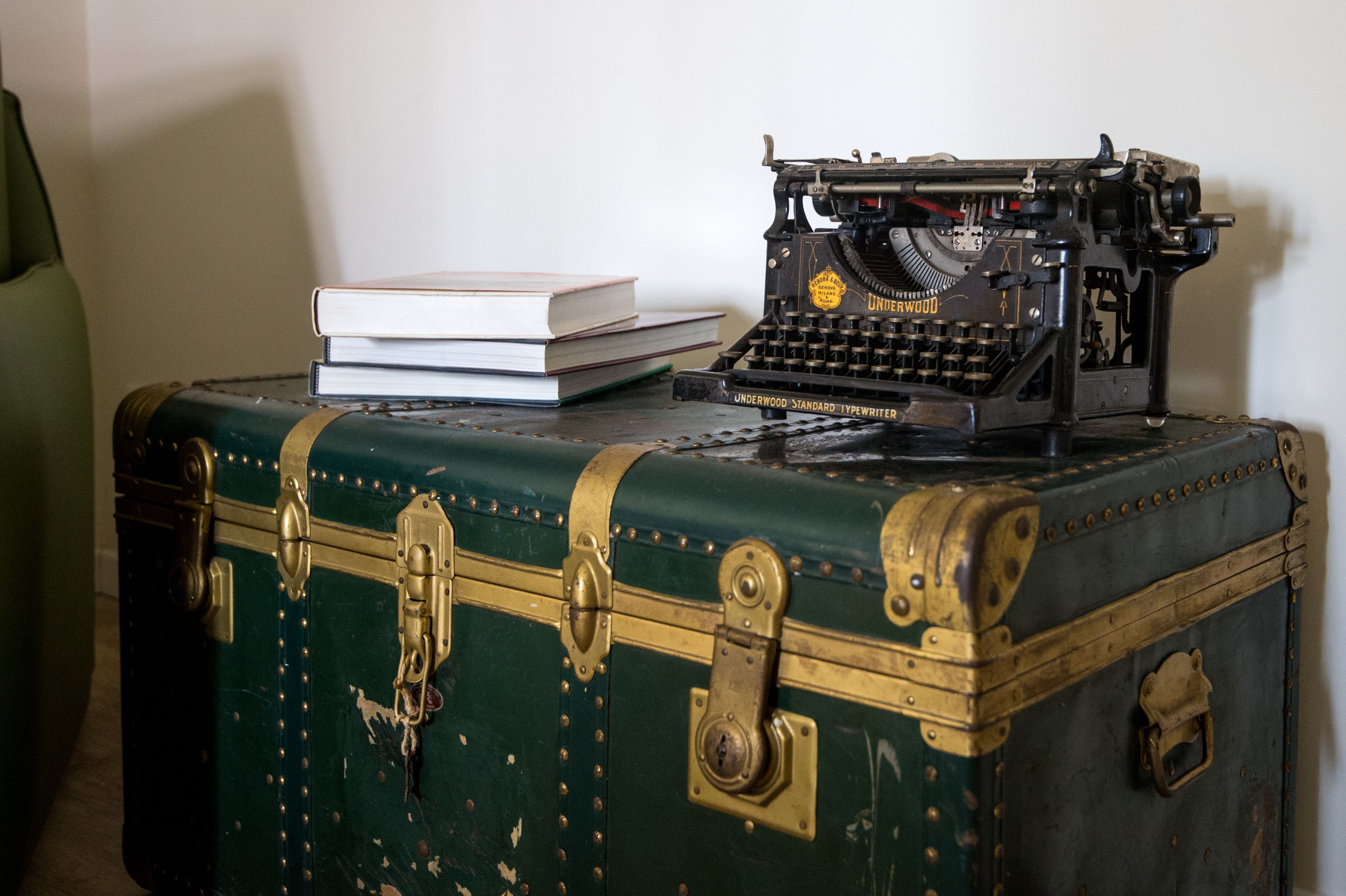 A vintage Underwood typewriter on a green suitcase with brass accents, accompanied by a stack of books.