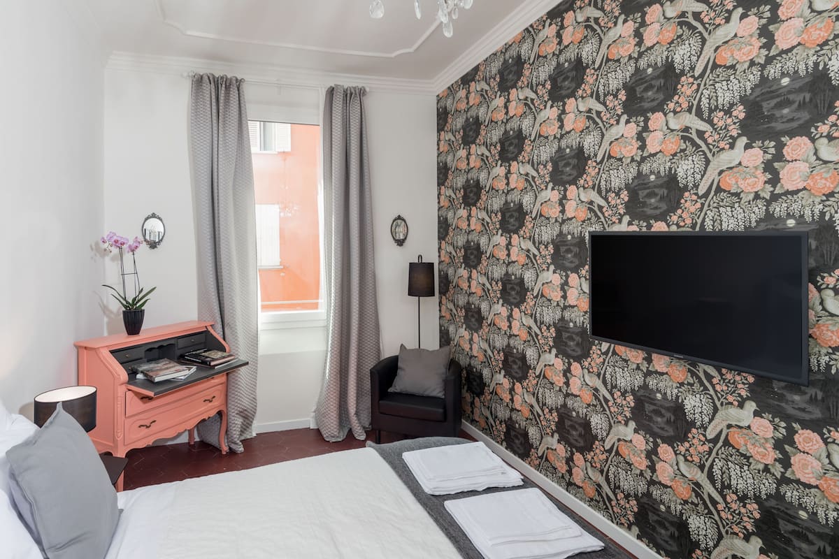 A hotel room with a bed, a dresser, a TV, and a window with curtains.