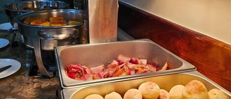 A buffet with various food items including bread rolls and cooked meats.