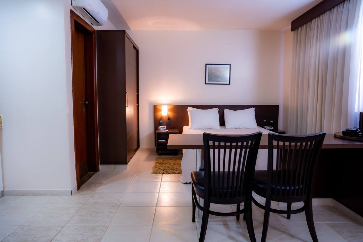 A hotel room with a bed, bedside table, lamp, and two chairs.