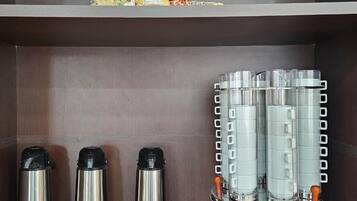A hotel room with a shelf displaying a religious statue, a coffee station with multiple coffee makers, and a tray with stacked plates and a cup.