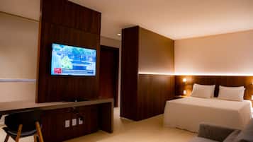 Una habitación de hotel con un escritorio de madera, un televisor en la pared, una cama con ropa de cama blanca y una mesita de noche con lámpara.