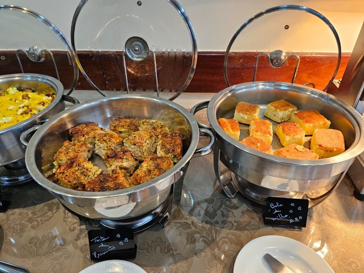 Ein Buffet mit verschiedenen Speisen in Metallbehältern, darunter eine Auflaufform und Brot.