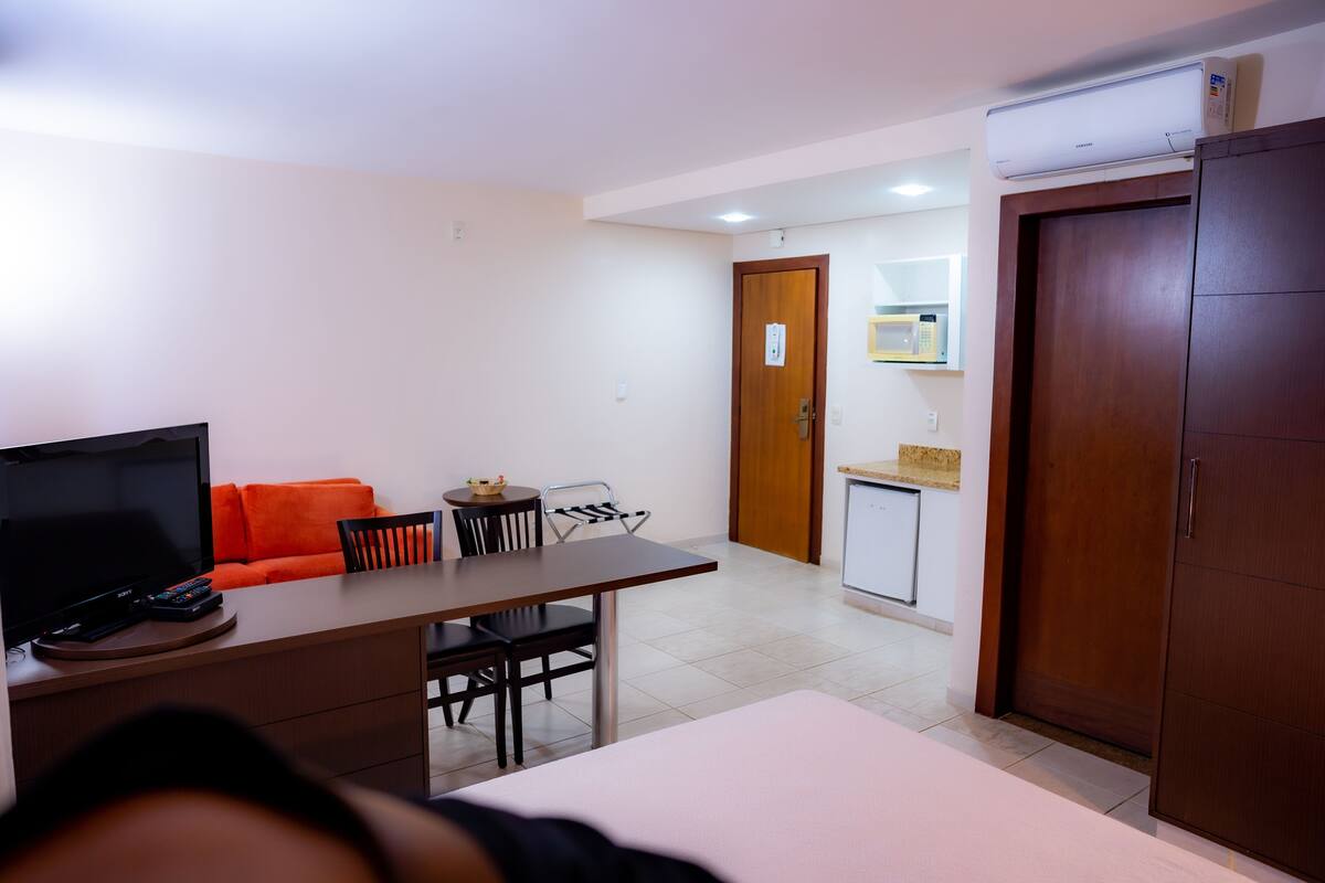 A room with a bed, a TV, a desk, a chair, a small table, and a sofa.