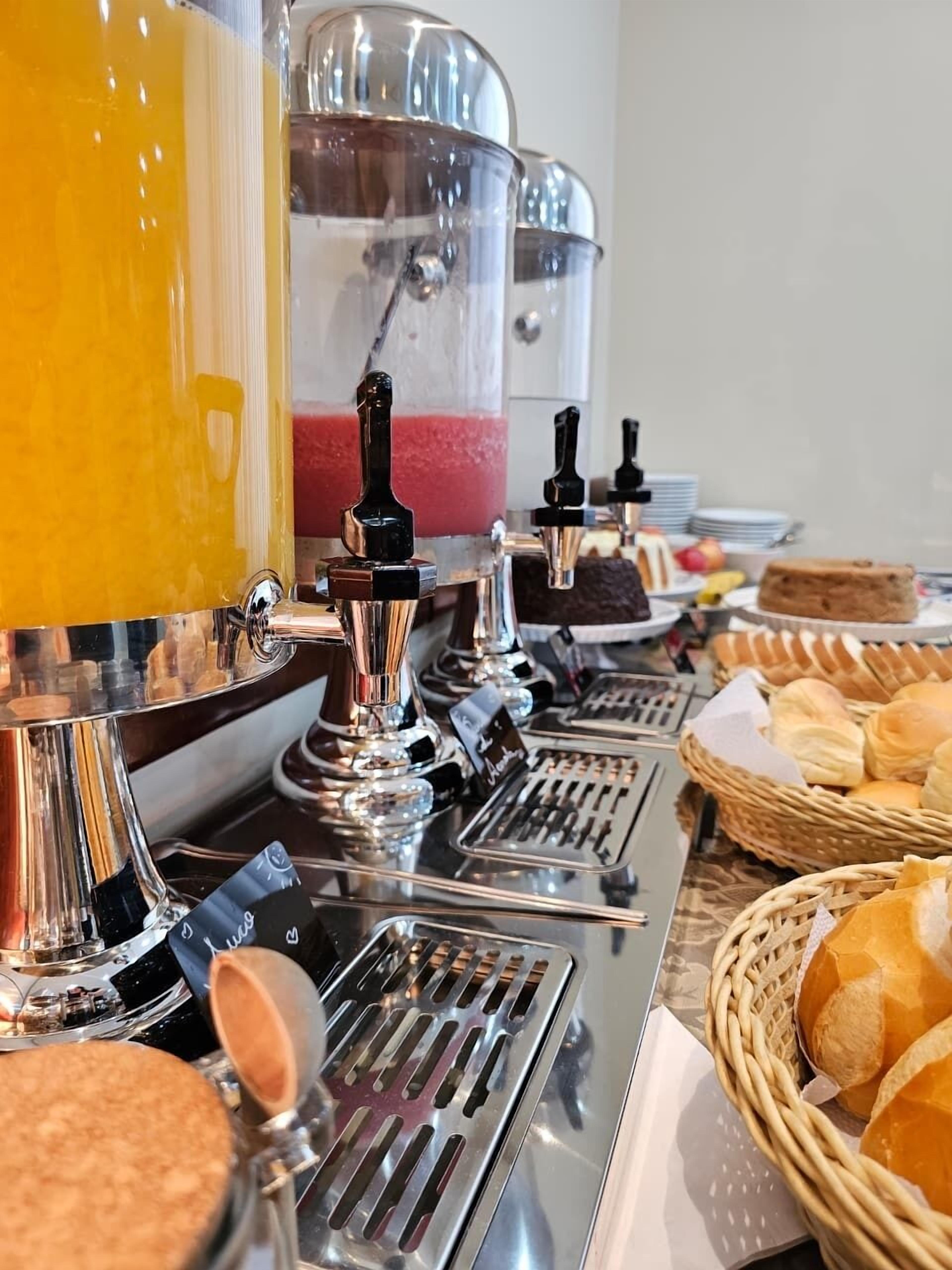Una estación de café con varias máquinas de espresso, un dispensador de jugo y una variedad de pasteles y pan.