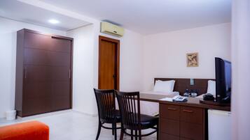 Quarto de hotel com escrivaninha, duas cadeiras, uma cama, televisão e guarda-roupa.