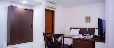 Una habitación de hotel con escritorio, dos sillas, cama, televisor y armario.