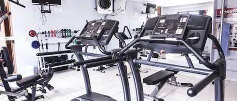 Un gimnasio con cintas de correr, máquinas de pesas y una televisión instalada en la pared.