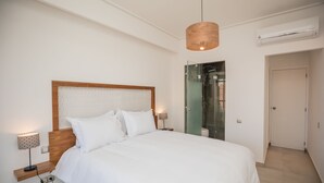 Un dormitorio moderno con cabecera de madera, una cama grande, lámparas de noche y una cabina de ducha de vidrio.