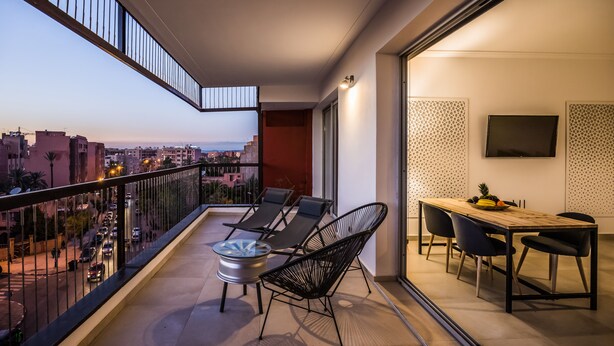 Un balcón con una mesa y sillas, un televisor montado en la pared y vistas a la ciudad.