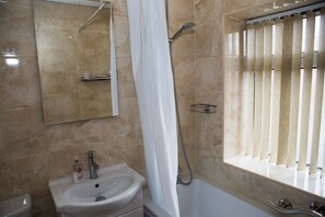 Baño con lavamanos, espejo, ducha y ventana con persianas.