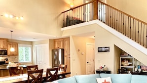 Un salón comedor amplio con un sofá seccional azul claro, una zona de comedor con sillas de madera, una cocina con armarios de madera y una escalera que sube a un nivel superior.