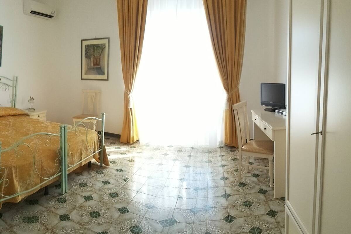 A bedroom with a bed, a desk, a chair, and a television.
