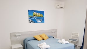 Ein ordentlich eingerichtetes Schlafzimmer mit einem Bett, einem Sessel, einem Nachttisch und einem Bild an der Wand.
