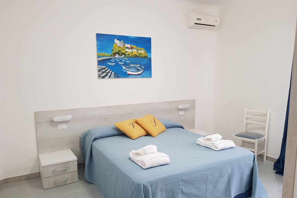 A neatly arranged bedroom with a bed, a chair, a nightstand, and a painting on the wall.