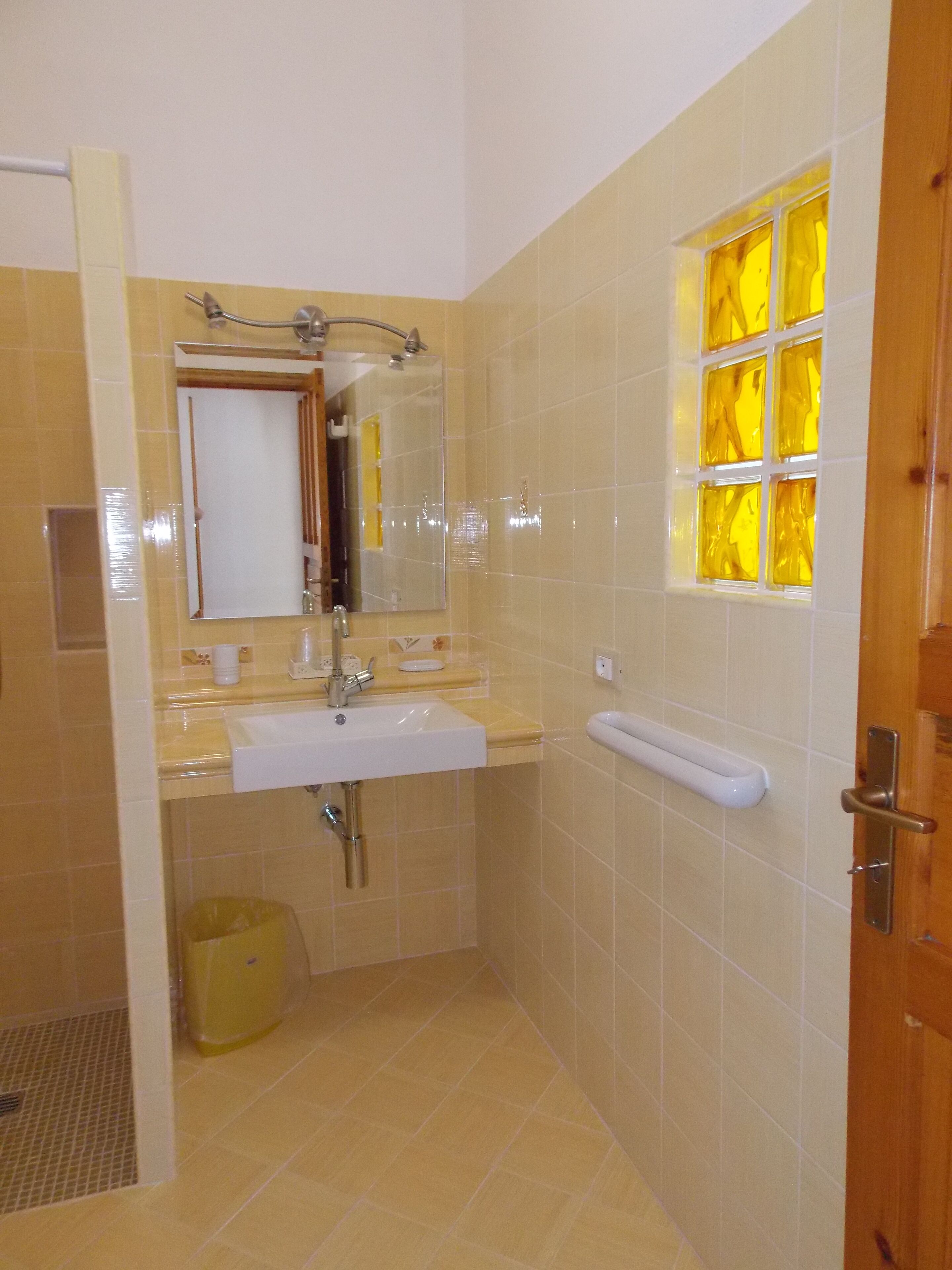 A bathroom with a sink, mirror, and a window with yellow-tinted glass.