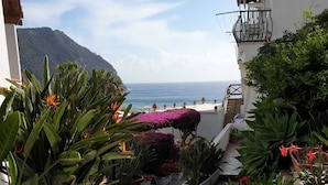 Ein schmaler Pfad führt zu einem Balkon mit Topfpflanzen und Blick aufs Meer.